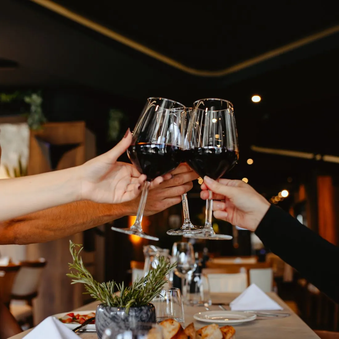 Četiri čaše crnog vina u nazdravljanju iznad stola